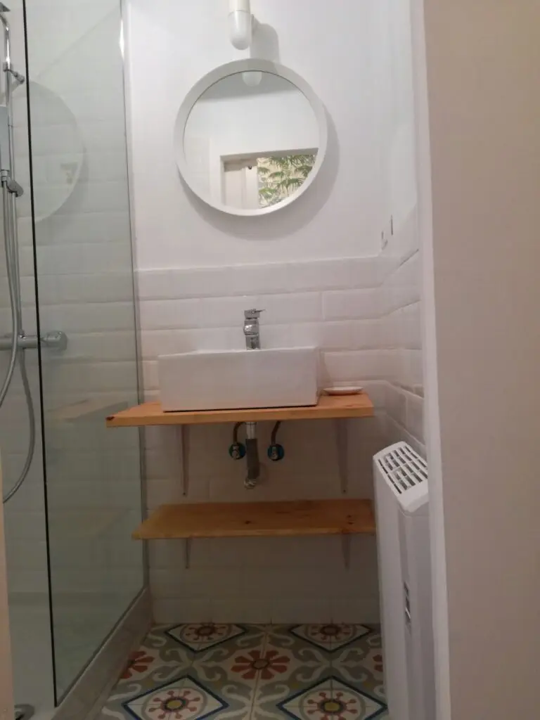 Baño con azulejo blanco tipo metro, espejo redondo y suelo de baldosa hidráulica en una vivienda reformada en Lavapiés, Madrid
