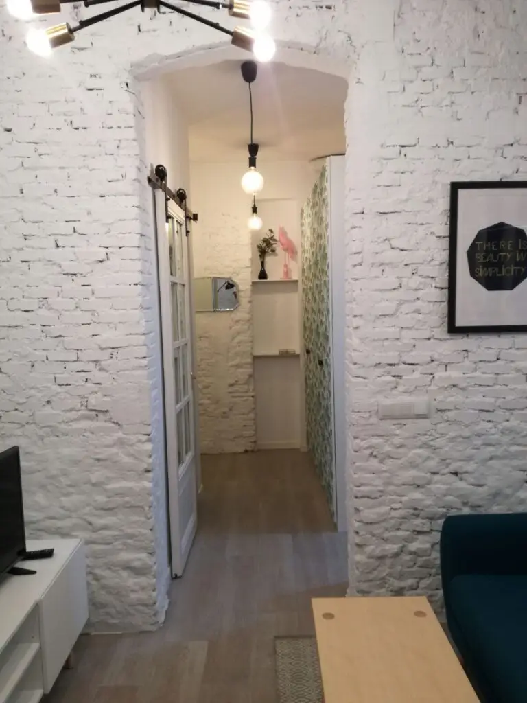 Salón con paredes de ladrillo pintado de blanco, puerta corredera y suelo de madera tras una reforma de diseño en Lavapiés, Madrid