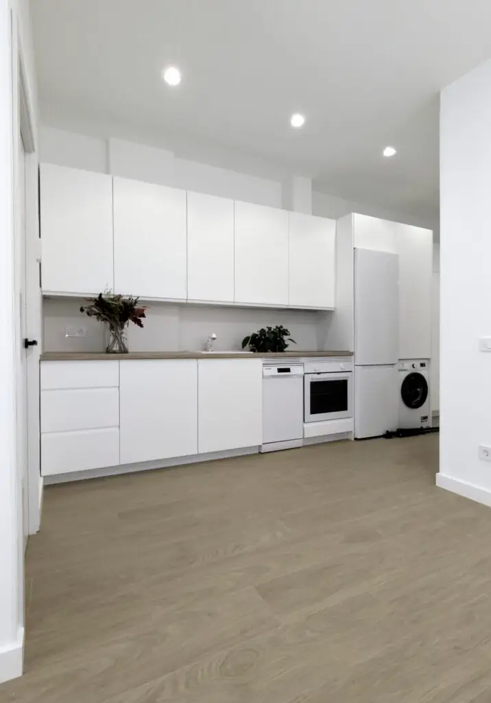 Cocina blanca integrada en el salón tras la reforma de un piso de 56 m² en Legazpi, Madrid