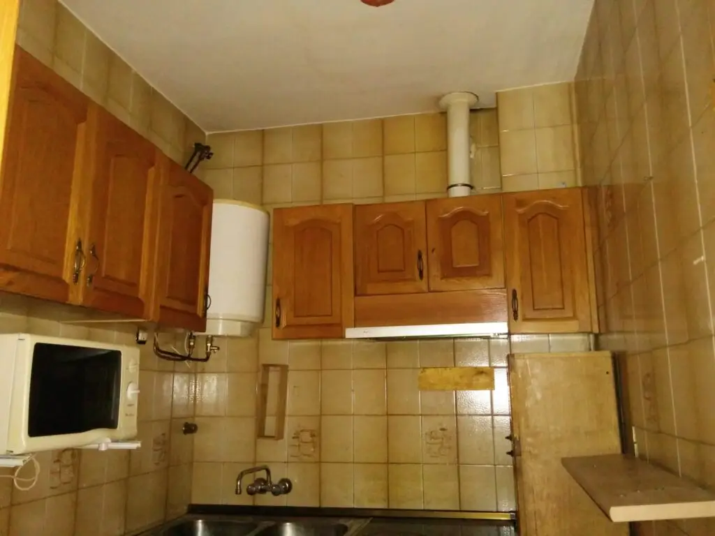 Cocina antigua con muebles de madera y azulejo desgastado antes de la reforma del piso en Madrid
