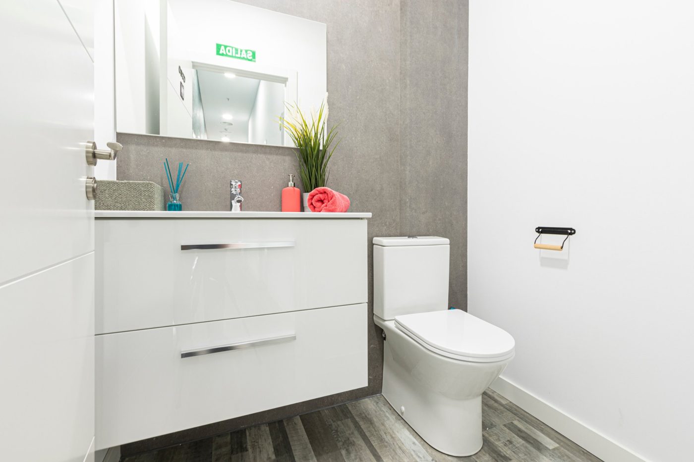 Aseo de un centro de estética en un centro comercial de Vallecas, con mueble de lavabo blanco y revestimiento gris