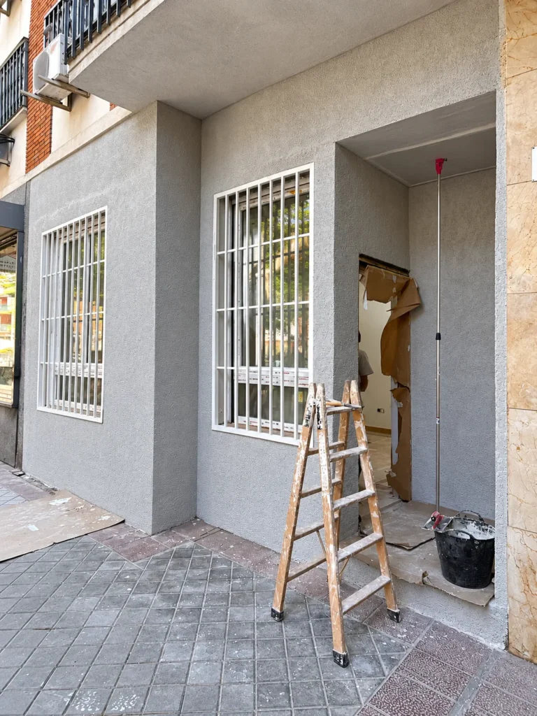 Fachada del local durante la obra, ya con ventanas con reja y una escalera de mano en la puerta