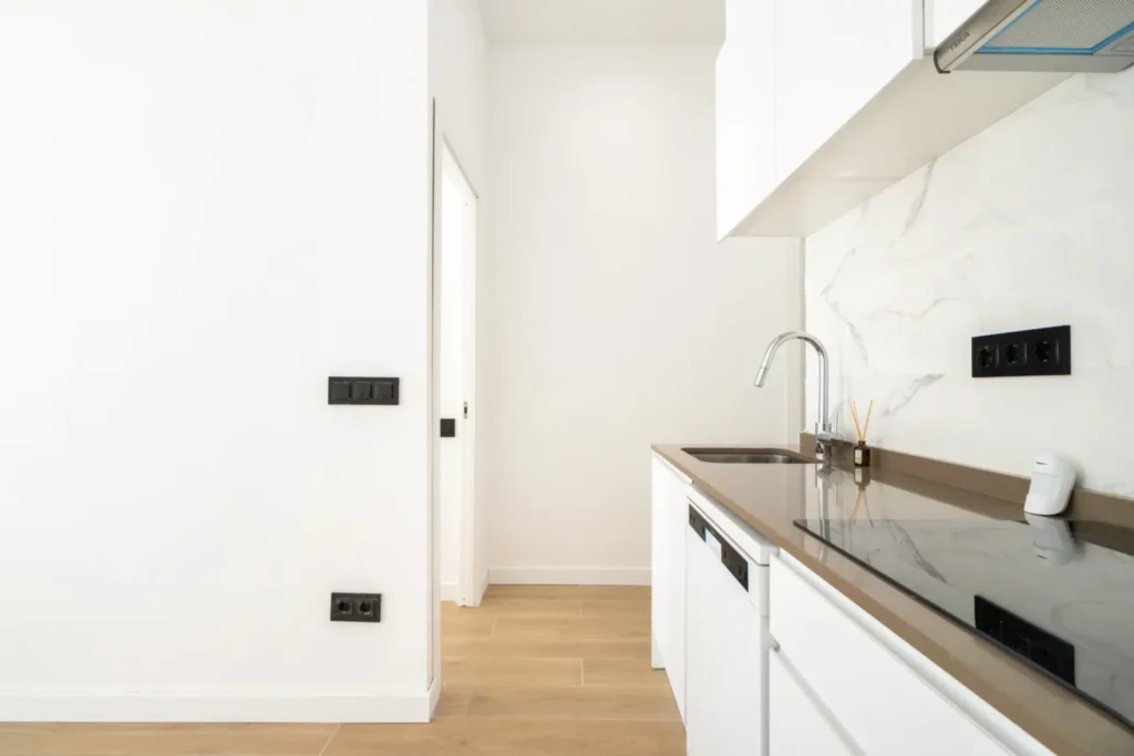 Cocina blanca lineal con encimera oscura y frente de mármol claro en una de las viviendas