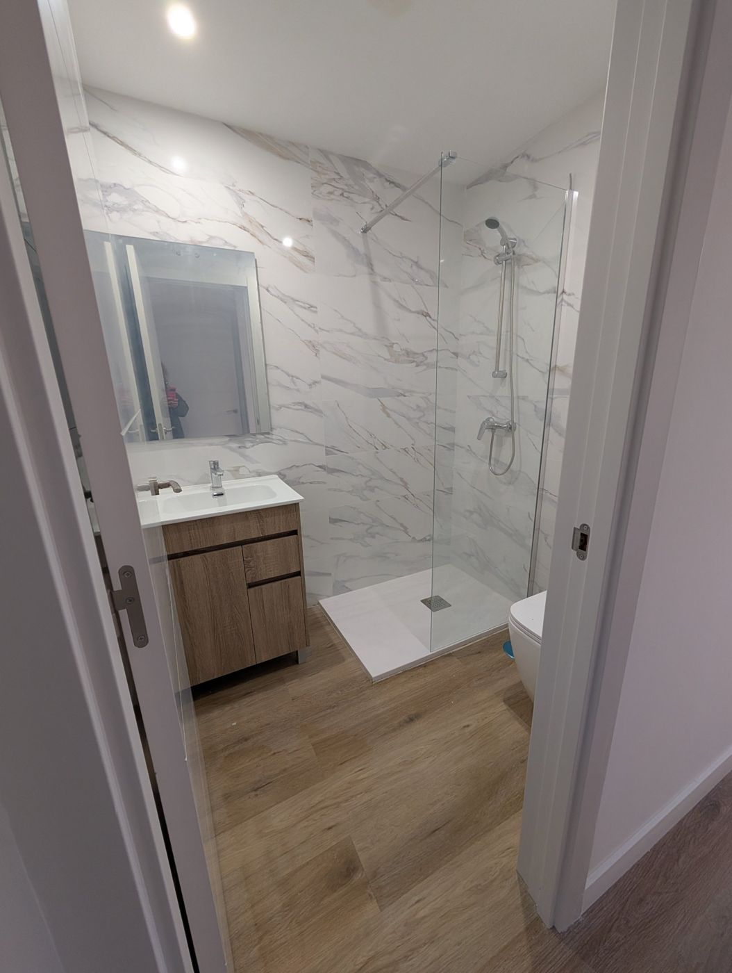 Baño reformado con plato de ducha y mueble de madera en una casa de huéspedes de Barrio del Pilar