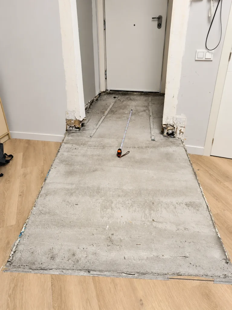 Pasillo en obra con el suelo de madera a medio colocar y una franja de solera al descubierto