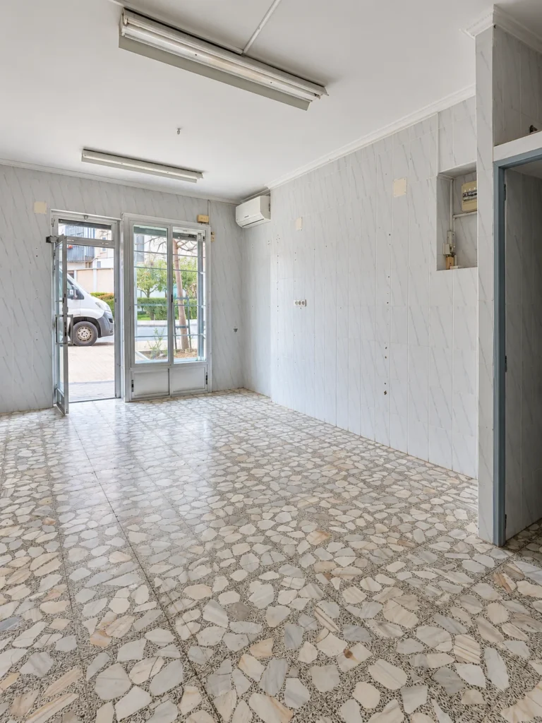 Interior del local antes de la obra, con suelo de baldosa antigua y paredes desnudas